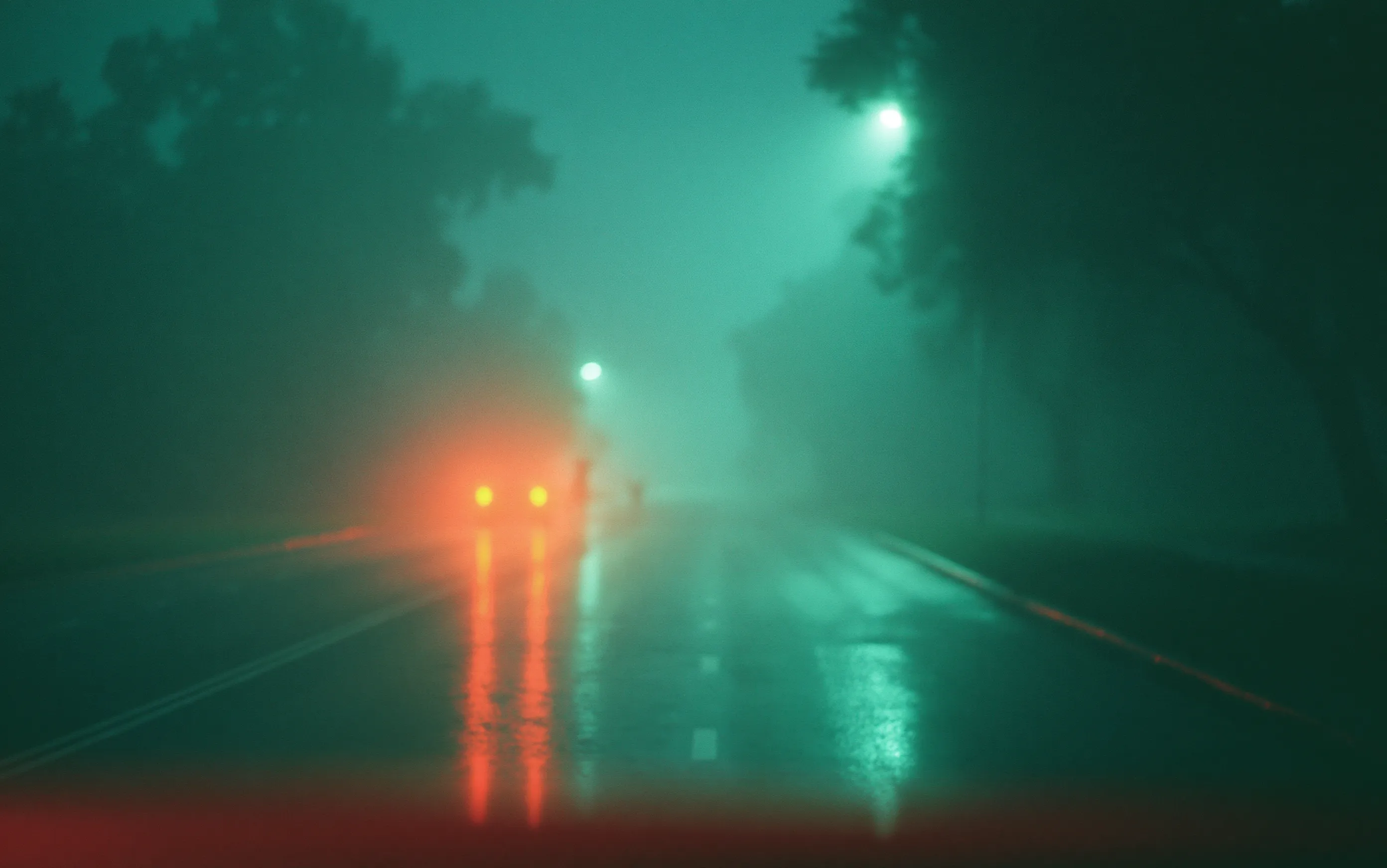 Rainy road at night with teal fog, a distant car and small amber lights